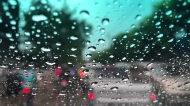 Araba ön camındaki yağmur damlasının odaklanmış görüntüsü, şehirdeki trafiği bulanıklaştırması, yağmur fırtınasında araba sürmesi, sokak lambasının renkli bokeh 'i, seçici odak noktası.