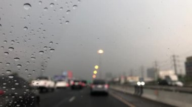Araba ön camındaki yağmur damlasının odaklanmış görüntüsü, şehirdeki trafiği bulanıklaştırması, yağmur fırtınasında araba sürmesi, sokak lambasının renkli bokeh 'i, seçici odak noktası.