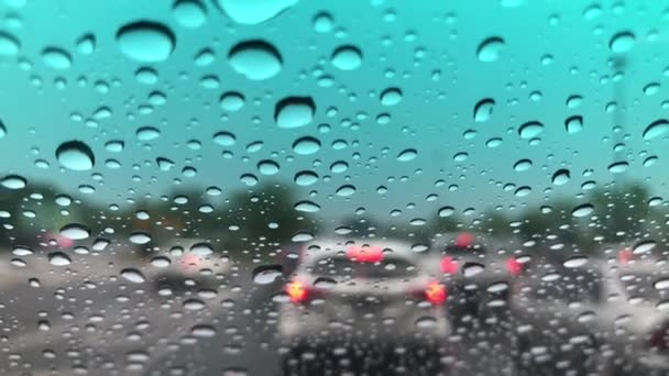 车辆挡风玻璃上的雨滴图像被破坏 城市道路上的交通状况模糊不清 暴雨中驾车 街灯的五彩斑斓 有选择的焦点 — 图库视频影像
