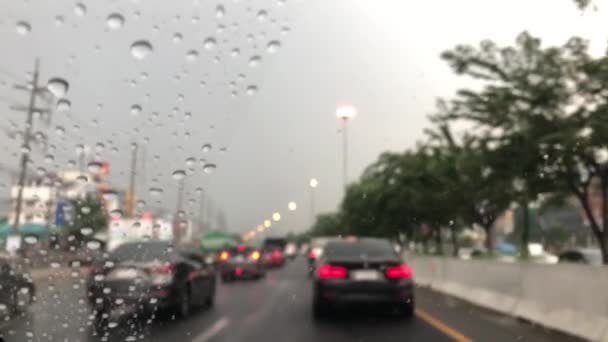 车辆挡风玻璃上的雨滴图像被破坏 城市道路上的交通状况模糊不清 暴雨中驾车 街灯的五彩斑斓 有选择的焦点 — 图库视频影像