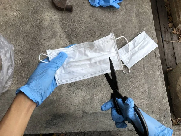 Human cutting used hygiene mask with scissor for prevented reuse before putting in trash bin,since it is a source of disease,coronavirus,bacteria and more from saliva.Concept of prevented of covid-19.