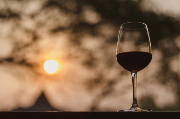 A glass of red wine on table with sunset background.