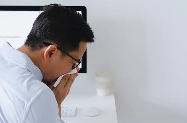 Asian man sneezing on napkin at working place for flu and virus concept.