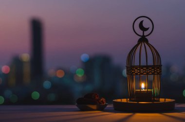 Üzerinde ay sembolü olan fener ve üzerinde alacakaranlık gökyüzü ve şehir arkaplanı olan küçük hurma tabağı kutsal Ramazan ayı Kareem 'in Müslüman ziyafeti için ışık saçar..