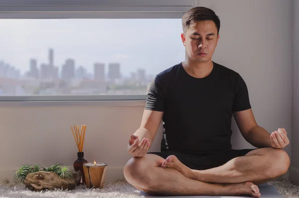 Mindful healthy mature asian man practicing meditation at home sitting on the floor doing yoga for mental balance relaxing on stress and enjoying time away from technology.