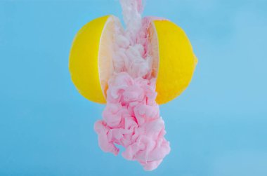 Yaz için mavi arka planda iki dilim limon arasında su damlasında pembe poster renginin çözünmesinin kısmi odak noktası, soyut ve arka plan kavramı.