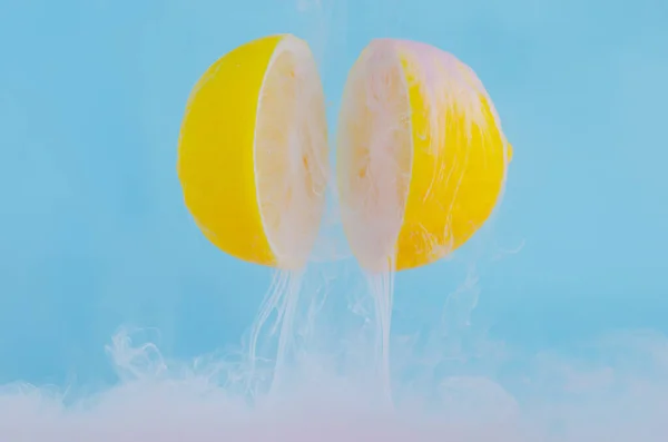 Blurred focus of dissolving pink poster color in water drop between two slice lemons on blue background for summer, abstract and background concept.