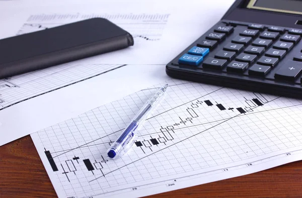 Masanın üzerinde bir hesap makinesi kalem makbuzu ve finansal tablo var.