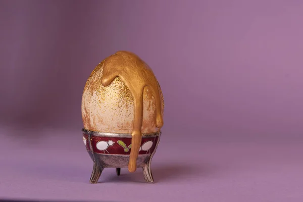 Işıltıdaki yumurta, mor arka planda altın bir gouache ile kaplanmış..