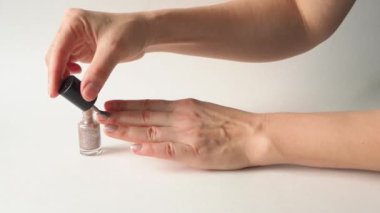 Eller beyaz arka planda ojeyle oje sürerler. Pullu Polonyalı. Bir fırçayla dikkatlice oje sürdüm. Güzellik salonlarının, kuaförlerin, manikürcülerin, manikürcülerin, manikürcülerin uzmanları.