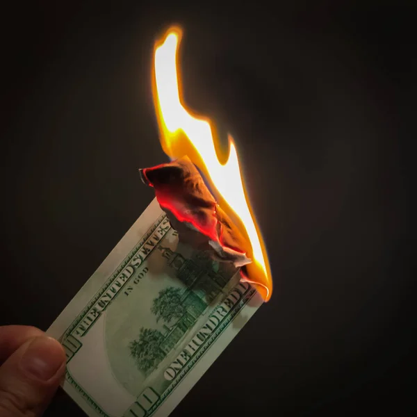 The hand holds a burning one hundred dollars. Illustration of the financial crisis and loss of money and capital. For news about exchanges, banks, insurance companies.