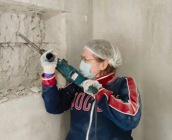 A girl in a mask and goggles punches a perforator through a niche in the wall.