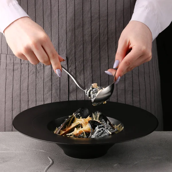 Kız İtalyan makarnası yiyor. Deniz mahsullü siyah makarna. Makarna kaşıkla çatalla yenir.