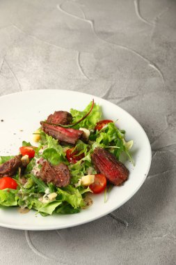 Biftekli salata kiraz domatesli peynir ve beton masa arkasında beyaz tabakta peynir..