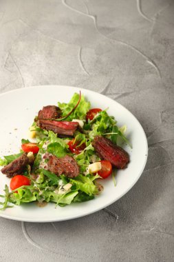 Biftekli salata kiraz domatesli peynir ve beton masa arkasında beyaz tabakta peynir..