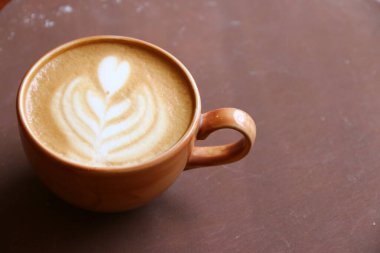 Kahverengi arka planda latte sanatıyla kapuçino..