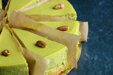 Çam fıstıklı cheesecake. Karanlık arka plan. Yeşil cheesecake bölümü tatlıyı yakın plan kesiyor.