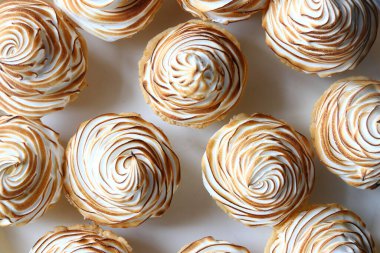 Beyaz arka planda kremalı limonlu tartlar, papatyalar bütün ve beyaz taştan bir zemin üzerinde taze limon dilimleri. Uzayı kopyala Düz yatıyordu