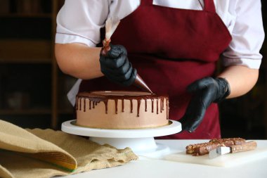 Pastanın üstüne çikolata. Şekerci, hamur torbasından kremalı bisküviye kadar sıvı çikolata sıkıyor.