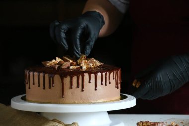 Şekerci masada çikolatalı pasta yiyor. Pastayı sıvı çikolatayla süsleme süreci. Koyu sırtlı çikolatalı pasta yapma süreci.