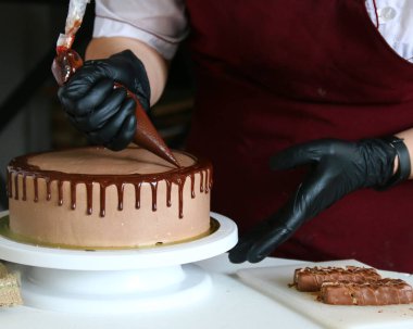 Pastanın üstüne çikolata. Şekerci, hamur torbasından kremalı bisküviye kadar sıvı çikolata sıkıyor.