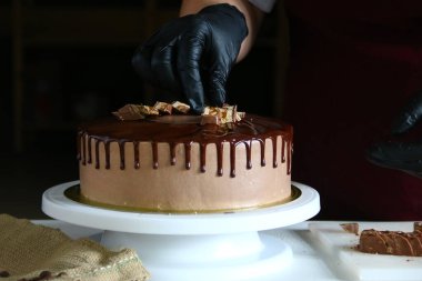 Şekerci masada çikolatalı pasta yiyor. Pastayı sıvı çikolatayla süsleme süreci. Koyu sırtlı çikolatalı pasta yapma süreci.