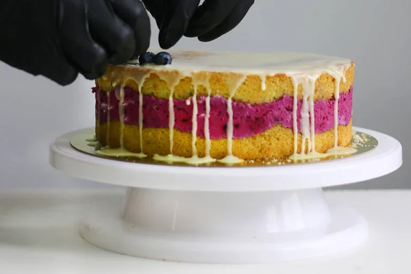 confectioner decorate blueberry cake. cake making process. dessert with confectioner hand on light back.
