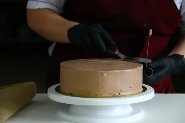Şekerci masada çikolatalı pasta yiyor. Pastayı sıvı çikolatayla süsleme süreci. Koyu sırtlı çikolatalı pasta yapma süreci.