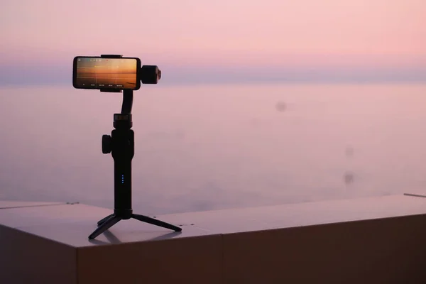 Yakın plan Smartphone bir deniz ve Mountians Peyzaj fotoğrafı ve video zaman ayarlı günbatımında Mobil Stabilizer standında