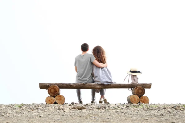 man hug woman and sitting on bench in mountain back view. love couple concept. man hug woman sitting on bench.the mountains are covered with cloud or fog. guy and girl hug embracing each other