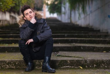 Kameraya bakarak sokakta oturan genç güzel adam,
