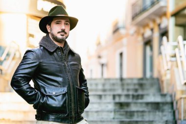 Şapkalı ve ceketli olgun bir adam elinde fotokopi makinesiyle merdivenlerde duruyor.