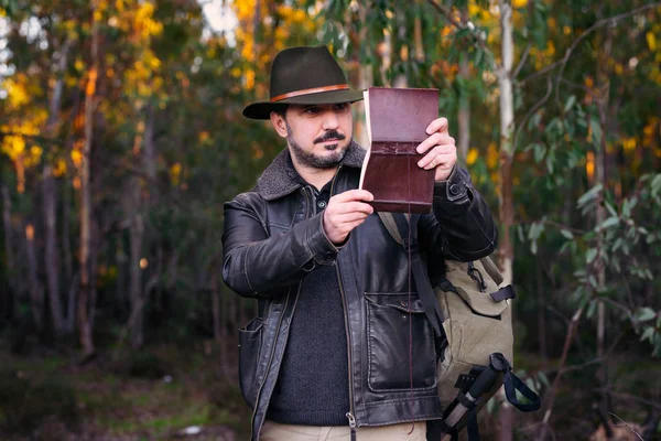 Gammal man med hatt och jacka ser gammal bok om skog med c — Stockfoto