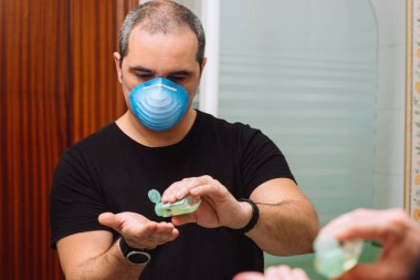 Yüz maskeli bir adam virüs mikroplarına karşı korunmak için dezenfektan dezenfektan kullanıyor.