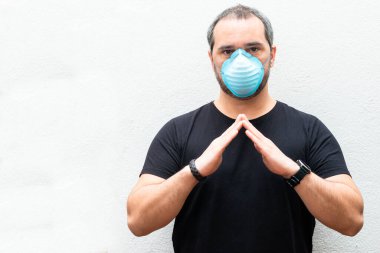 Tıbbi maskeli bir adam evin üzerinde el ele tutuşuyor. Evde kalma kavramı, karantina.