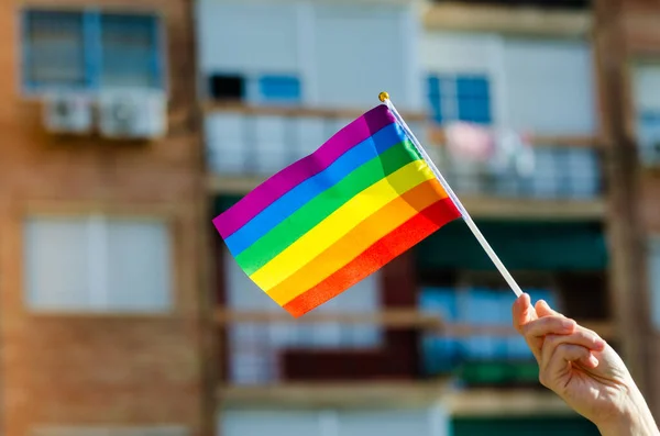 hand holding the flag of pride with the city blured in the background