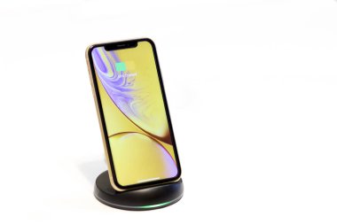 PORTLAND, OR / USA - 31 Mart 2020 - Elmanın kablosuz şarj teknolojisini kullanarak şarj olan sarı bir iPhone XR. Ekranda yarım şarjlı pil gösteren simge.