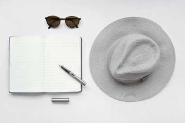Güneş gözlüğü, defter, kalem ve beyaz zemin üzerine şapka