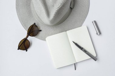 Güneş gözlüğü, defter, kalem ve beyaz zemin üzerine şapka