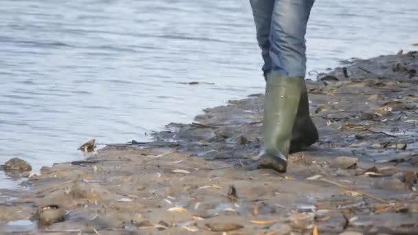 Egy férfi halász zöld gumicsizmában sétál a víztározó mocsaras partján. — Stock videók