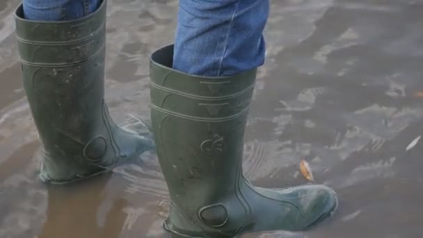 Een man visser in groene rubberen laarzen staat aan de oevers van een moerassige vijver — Stockvideo