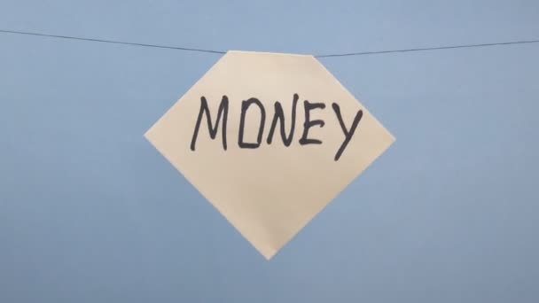 Ένας άντρας κρεμάει ένα λευκό φύλλο χαρτί με μια μαύρη επιγραφή χρήματα σε ένα μπλε φόντο — Αρχείο Βίντεο