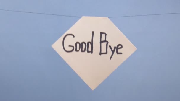 En man hänger ett vitt papper med en svart inskription adjö på en blå bakgrund — Stockvideo