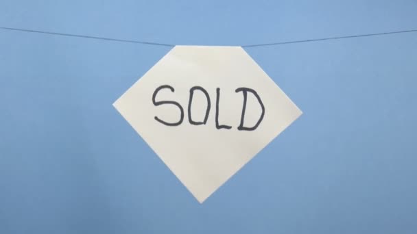 Hoja de papel blanco ardiente y humeante con una inscripción negra "vendida" sobre un fondo azul — Vídeo de stock