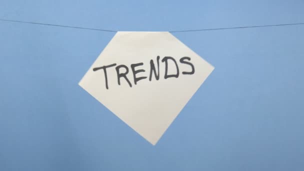 Brennendes und rauchendes weißes Blatt Papier mit der schwarzen Aufschrift "Trends" auf blauem Hintergrund — Stockvideo