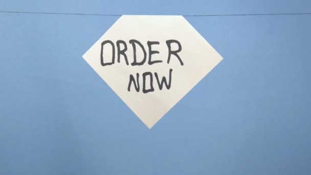 Brennendes und rauchendes weißes Blatt Papier mit schwarzer Aufschrift "Jetzt bestellen" auf blauem Hintergrund — Stockvideo
