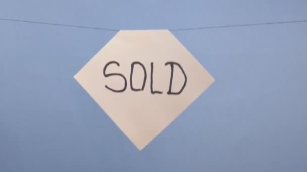 Мужчина вешает белый лист бумаги с черной надписью "продается" на синем фоне — стоковое видео