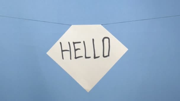 Mavi arka planda siyah bir "merhaba" yazılı beyaz kağıt yakmak ve tüttürmek — Stok video