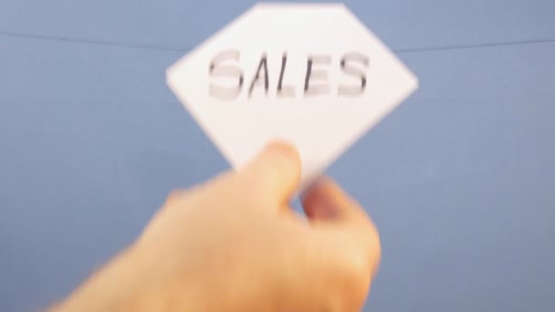 Um homem pendura uma folha branca de papel com uma inscrição preta "vendas" em um fundo azul — Vídeo de Stock