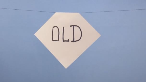 A man hangs a white sheet of paper with a black inscription "old" on a blue background — Stock video